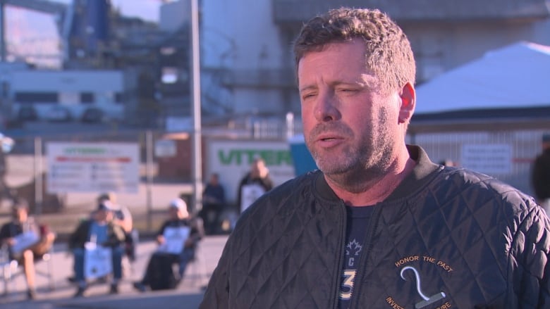 A man stands in front of a picket line and a grain terminal. 