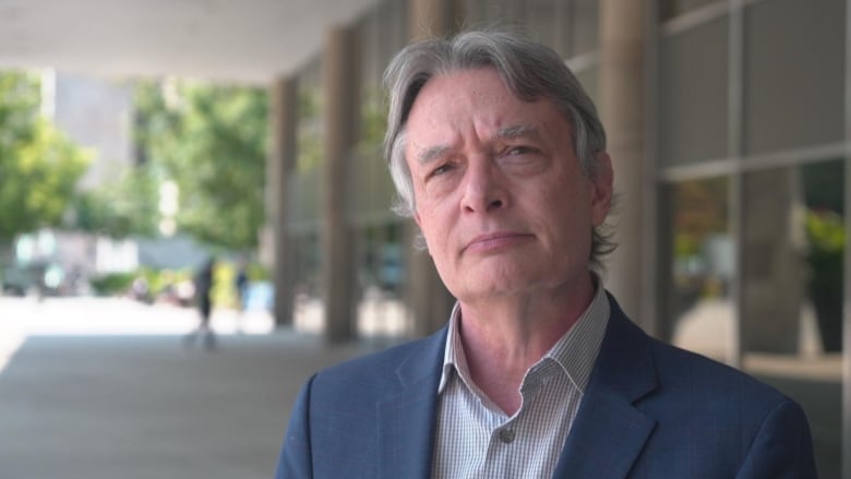 Gord Perks, a man with grey hair, wearing a blue suit jacket, stands outside the front door to Toronto's city hall. 