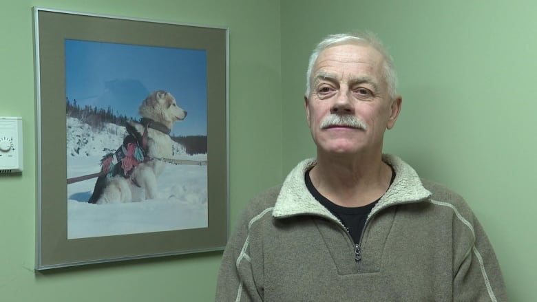 Peter Clarkson stands in front of a green wall with the photo of a polar bear behind him.