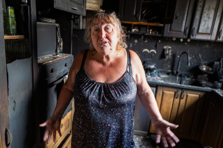 A woman in a blue dress stands in a destroyed home