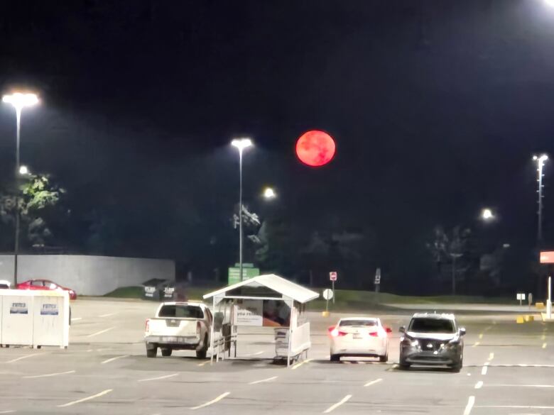 A full, red moon shines over a parking lot.