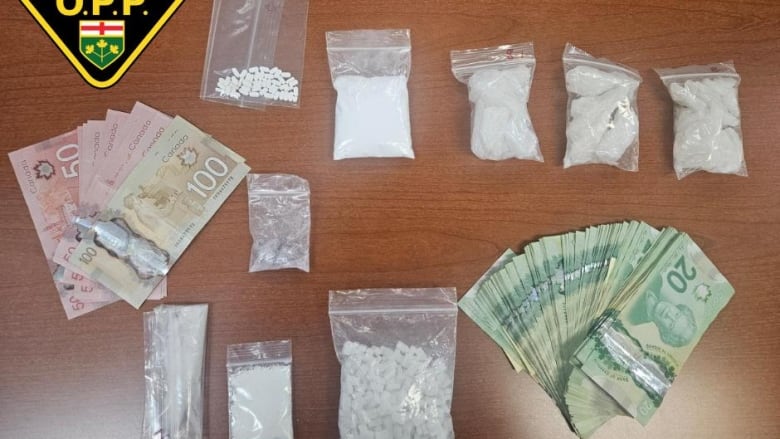 From left, several $50 and $100 bills are displayed on a table, beside various bags of white powder and pills and a handful of $20 bills to the right.