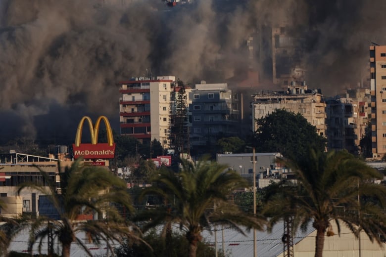 Smoke billows over a city after an airstrike. A McDonald's sign is also visible.