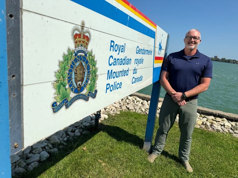 Ian Smith standing next to an RCMP sign with the Detroit River in the background.