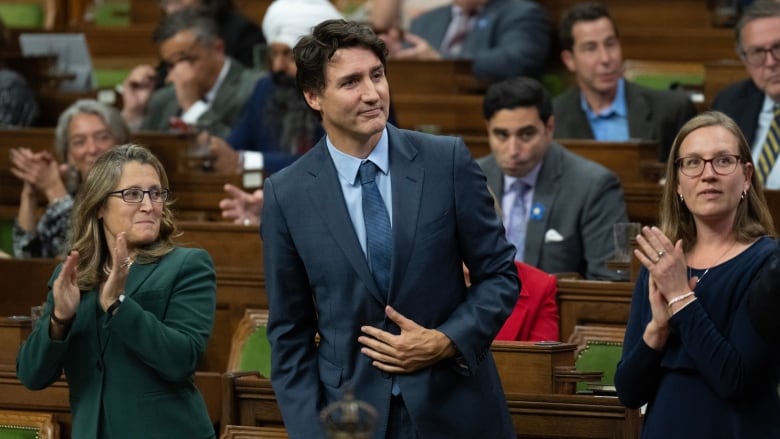 A man in a grey suit stands in the House of Commons as those around him applaud.