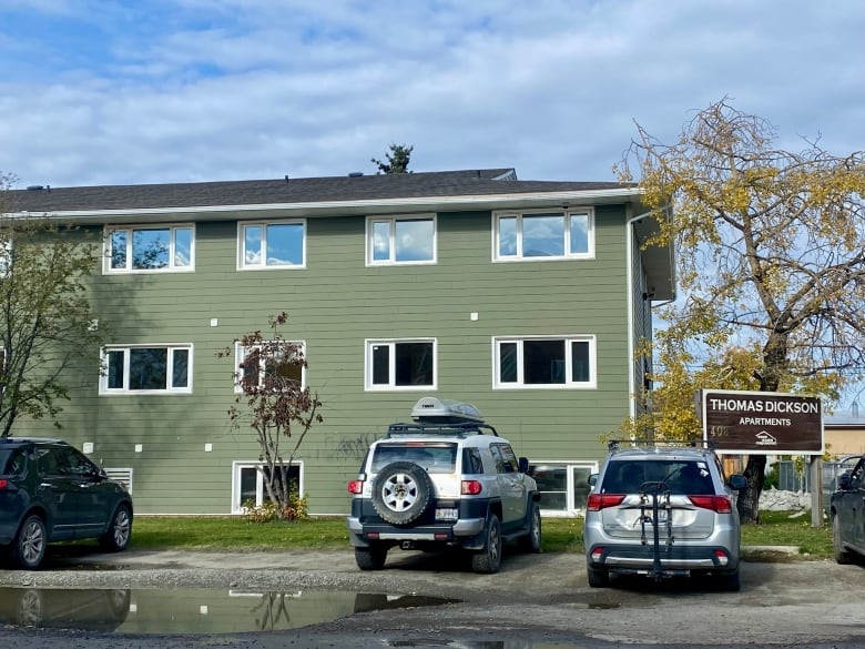 Cars parked in front of a green, 3-storey apartment building.