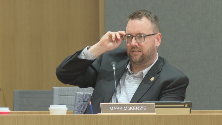 A man wearing glasses in a municipal government room.