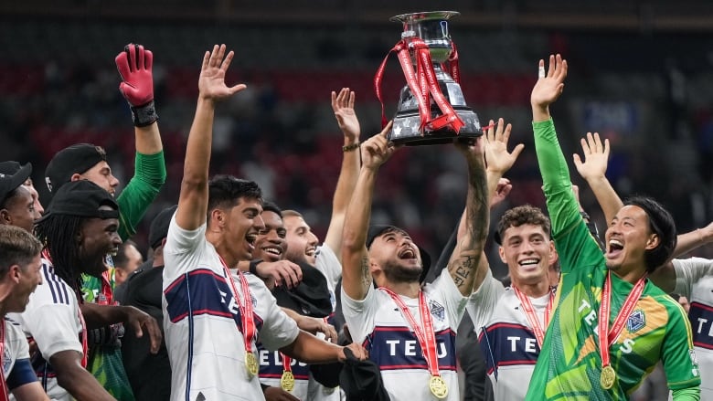 A group of soccer players celebrate as they hoist a trophy in the air.