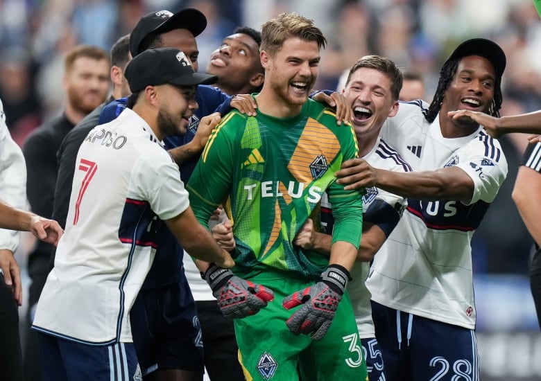 A group of soccer players smile and celebrate in a group.