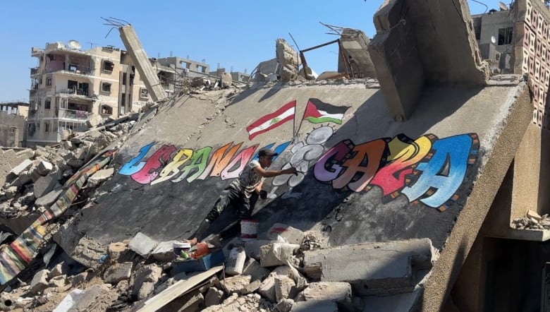 A man paints a mural on a concrete slab after an airstrike. The colourful mural has the words 