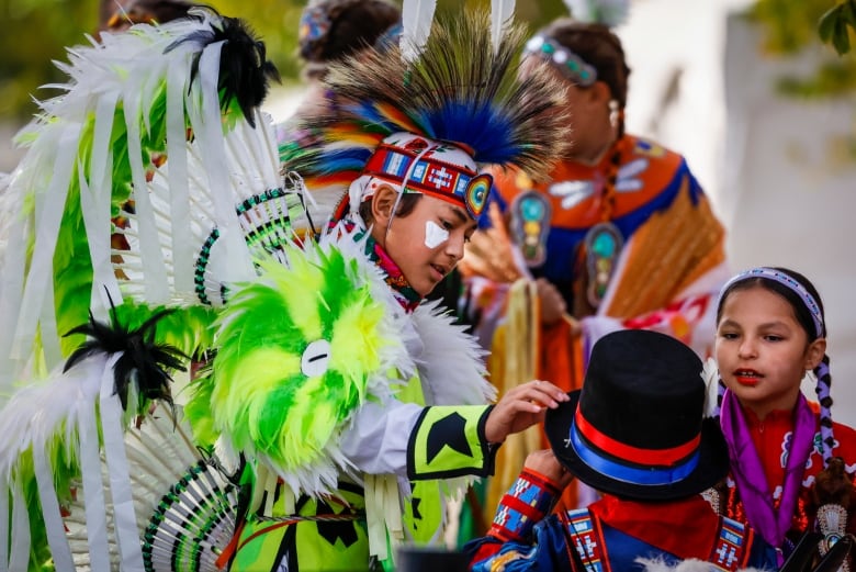 an Indigenous dancer puts a hat on a small child.