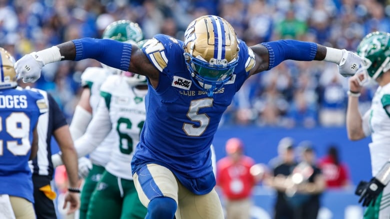 A football player in a blue jersey spreads his arms wide in celebration.