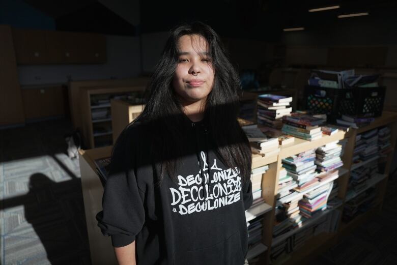 A student wearing a black hoodie stands in a library at Poplar River School.