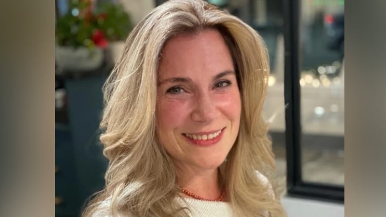 A woman with blonde hair stares at the camera with a smile.