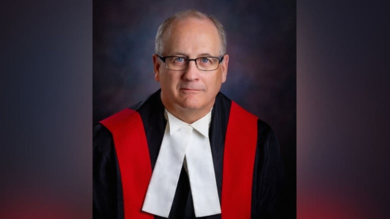 A portrait of a man wearing a black and red robe with a white bib.