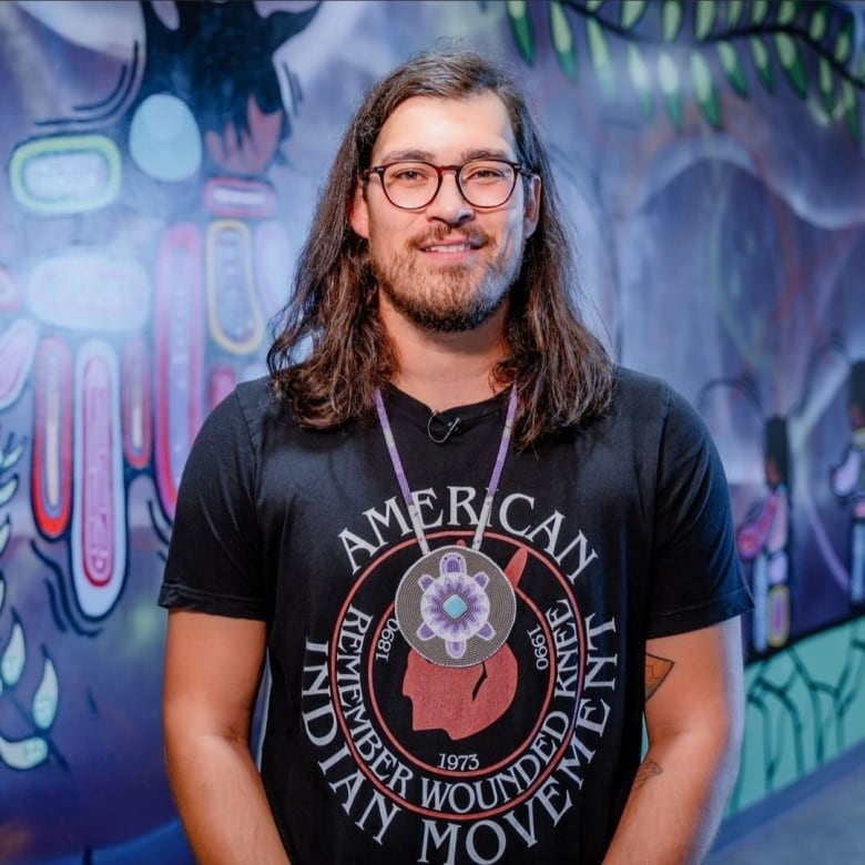 A man stands in front a mural, smiling at the camera.