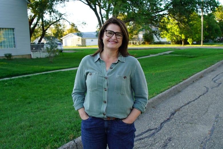 A woman in a collared button up shirt and jeans on a residential street