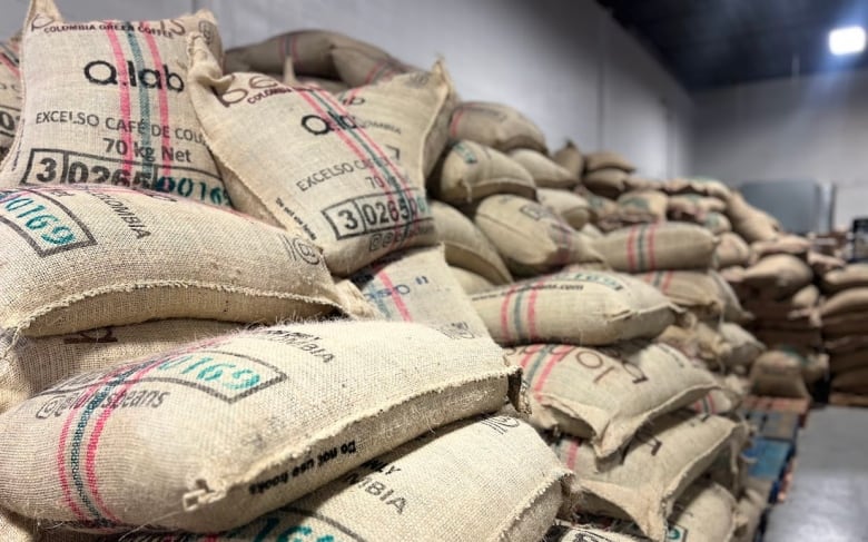 Numerous burlap bags of coffee are stacked up on top of each other. 