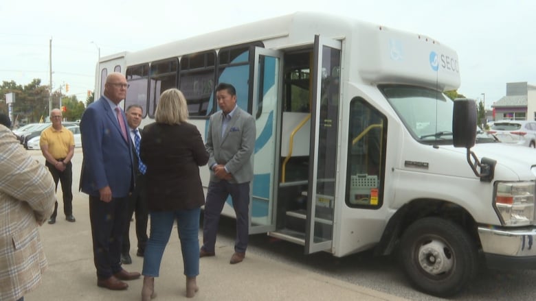 A group of people in conversation outside a shuttle bus.