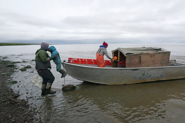 People getting onto a small boat on a rocky shore.