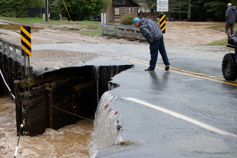 A person leans over the survey a collapsed portion of a bridge.