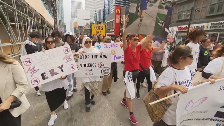 A large crowd with anti-gun-violence signs march along a city street in Toronto during a grey day