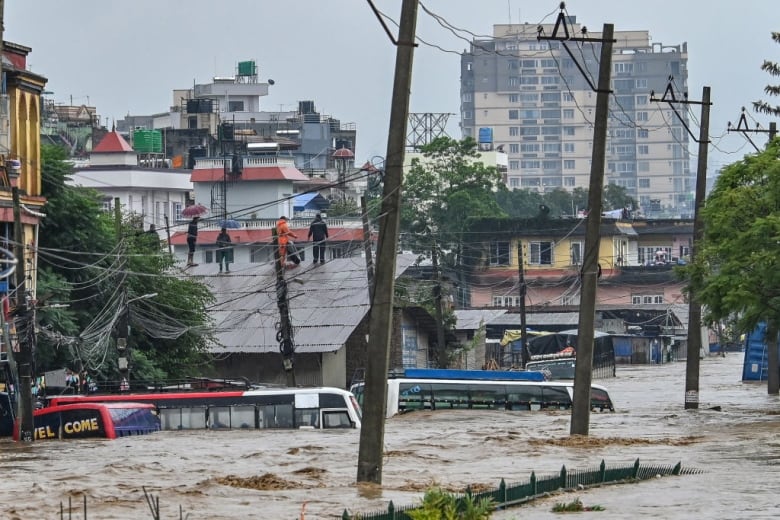 Residents climb over a rooftop to escape floodwaters, which cover most of two buses. 