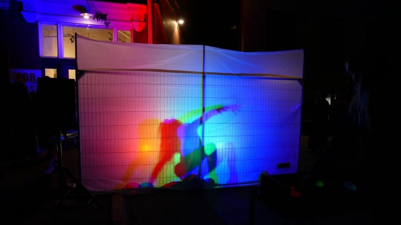 A person moves their body behind a multi-coloured screen during an art performance. 