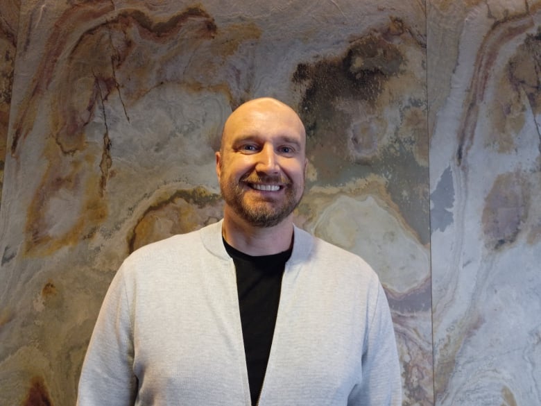 Man in white sweater and black shirt, smiling.