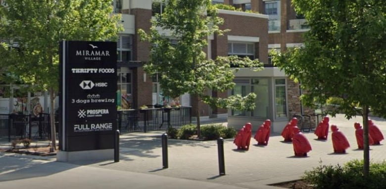 An image showing a sign reading 'Miramar Village' with a number of commercial tenants, next to an art installation depicting eight red crouching men.