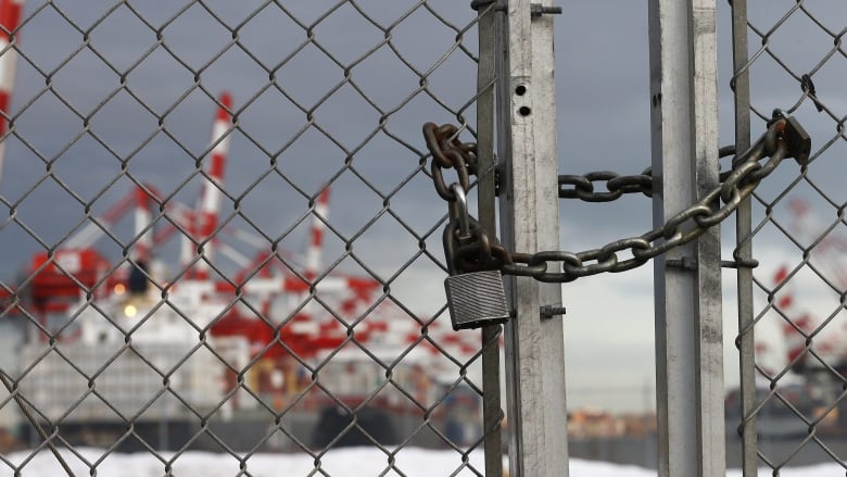 A padlocked gate is seen in the foreground as a container ship is seen in the background. 