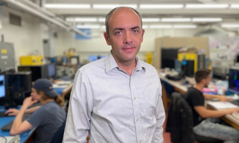 A man in a collared shirt stands in a laboratory where students are working.