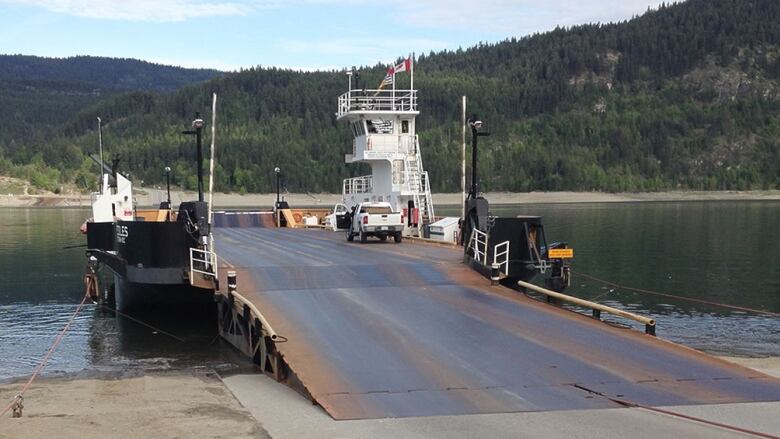 a single-deck ferry is docked on the shore, its ramp is out and touching the road