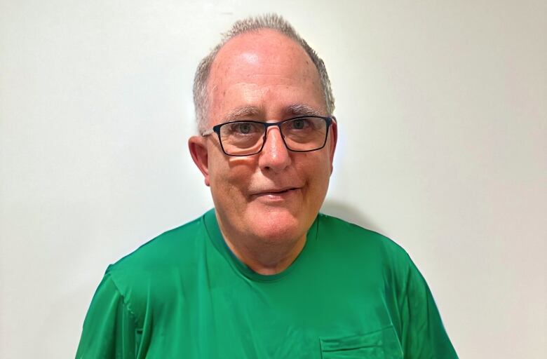 A man in a green shirt standing in front of a white background.