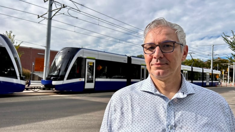 A man in a blue shirt and black glasses stands near a passing LRT train. 