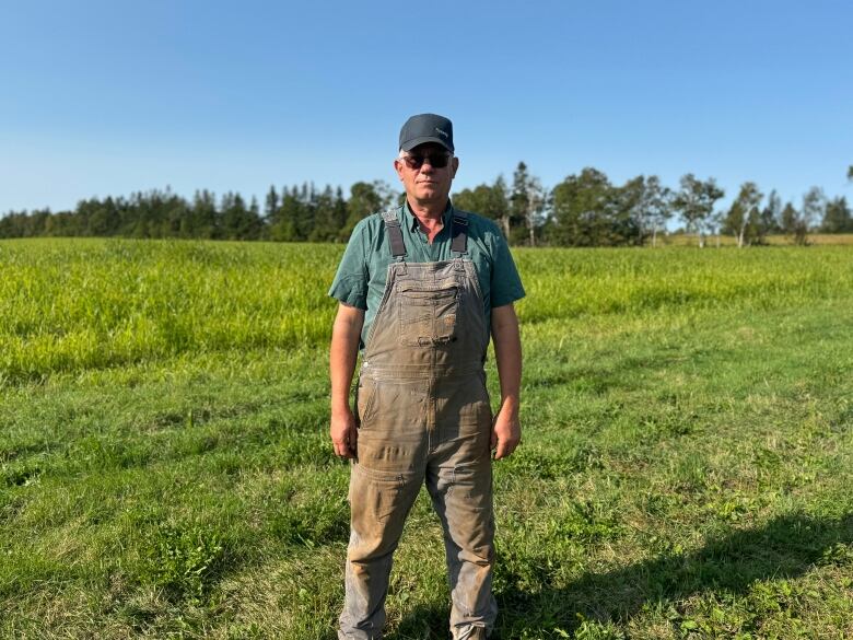 Man in dirty overalls standing in field.