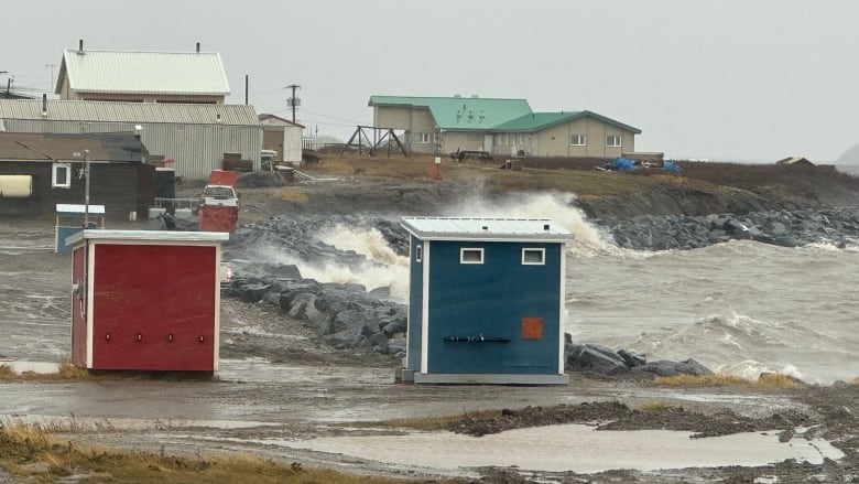 Red and blue shelters are seen on the coastline while waves crash on rocks.