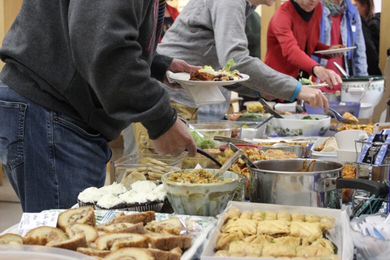 Food on a table and people filling plates.