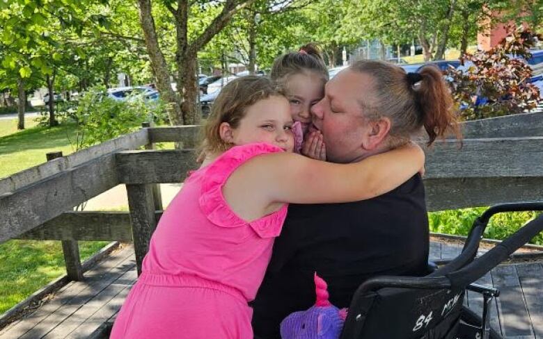 Whelan in a wheelchair with two children hugging her.