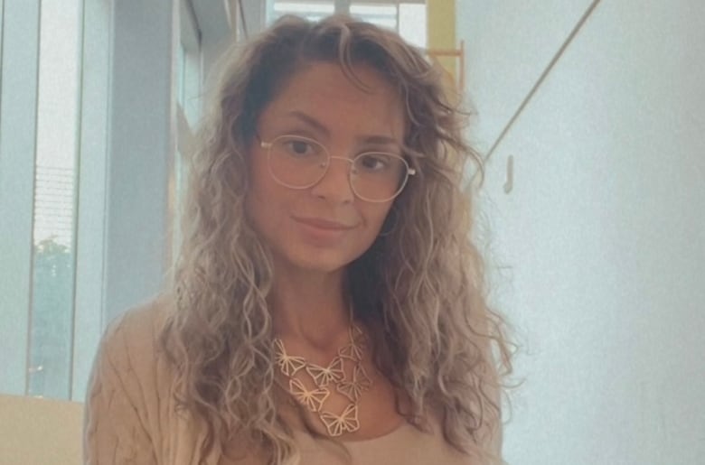 A woman with curly brown hair and glasses is smiling at the camera. 