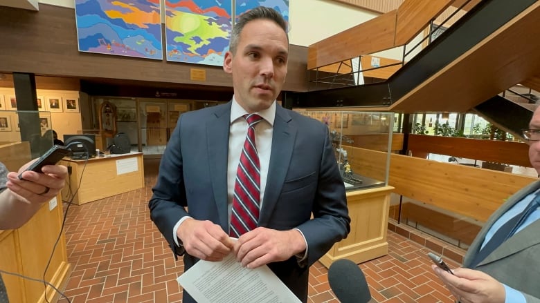 A man in a suit speaks with reporters.