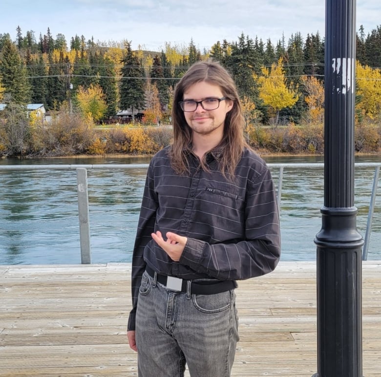 A young man stands in front of the Yukon River. 