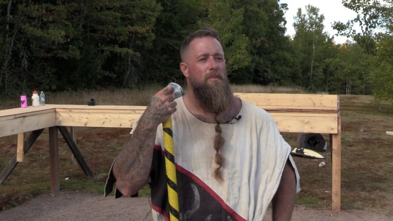 a man with tattoos holding a stick looks at the camera