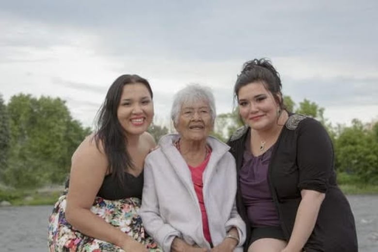 Three women sitting together smiling. Two are cousins, and the grandmother sits between them. 