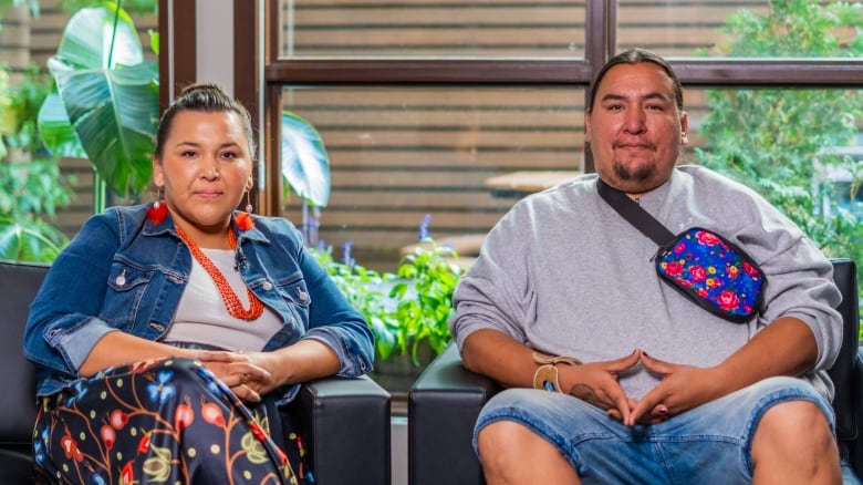 Two siblings sitting beside one another on chairs, the brother David makes a diamond shape with his hands. 