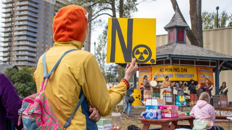 A person is seen from behind holding a sign that says 