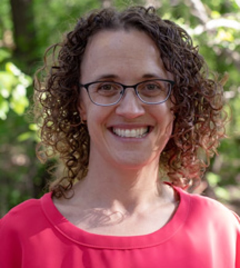 Tessa Penrod is wearing a pink shirt and glasses. She has curly brown hair and is smiling as she looks at the camera.