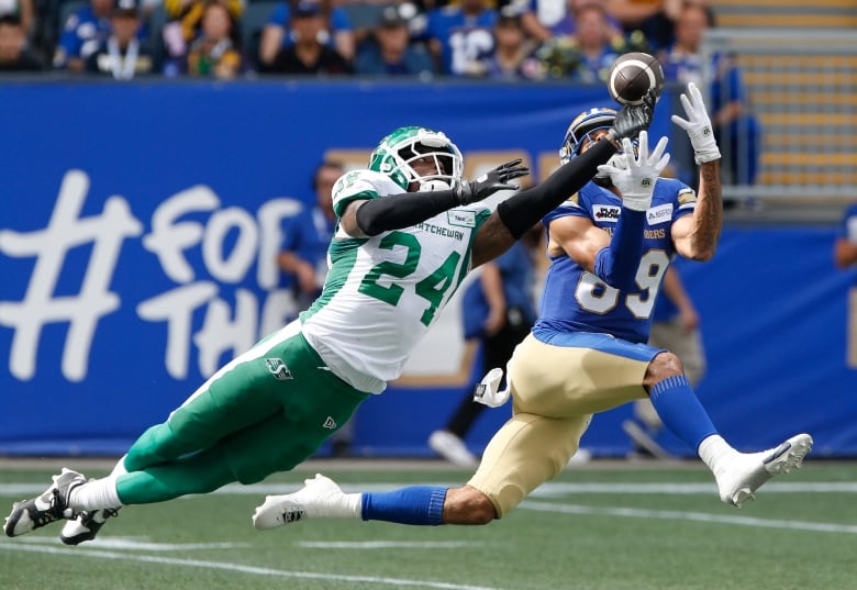 A Saskatchewan Roughrider player is seen knocking away as pass that is heading towards a Winnipeg Blue Bomber.