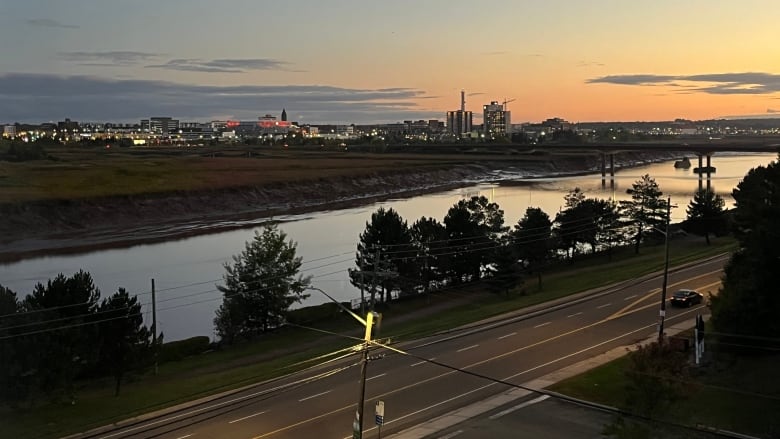 The sun rises over a river with a city skyline in the background.