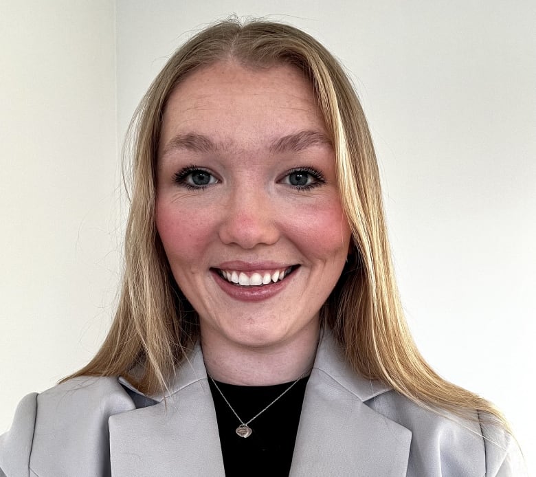 A young woman with long blonde hair and a grey blazer smiles at the camera.